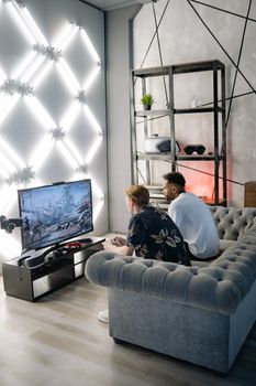 Two friends enjoy playing video games in a stylish, modern apartment setting with unique lighting.
