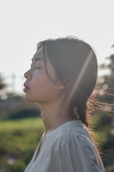 Side profile of a woman outdoors with eyes closed, basking in sunlight.