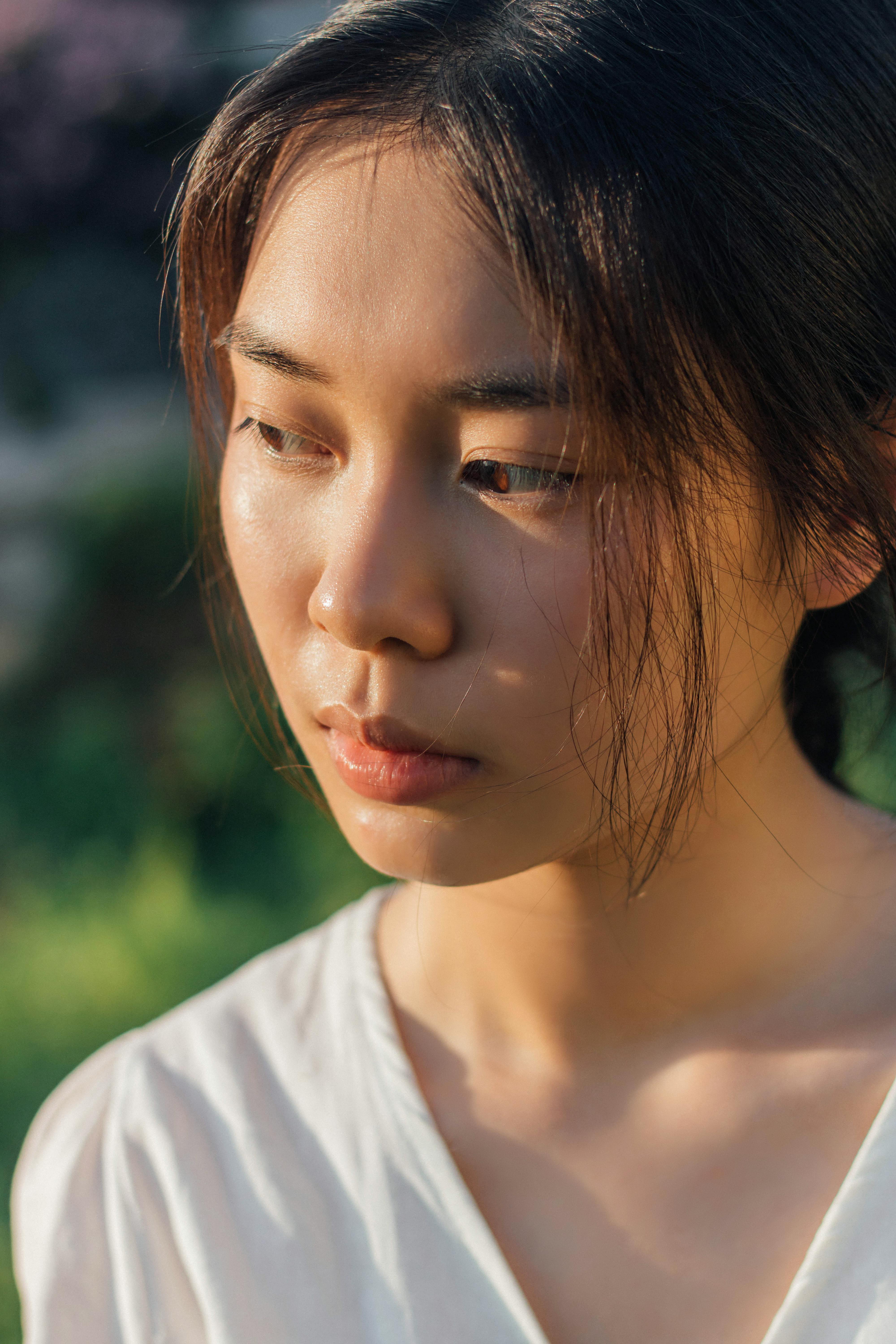 Close-up of a woman in soft sunlight, capturing a thoughtful expression outdoors.