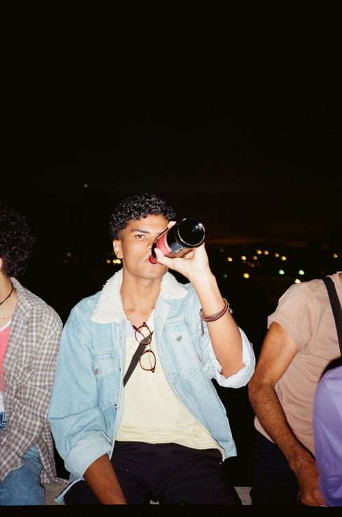 Free A young adult enjoys a drink from a wine bottle in an outdoor evening setting, adding a casual vibe. Stock Photo