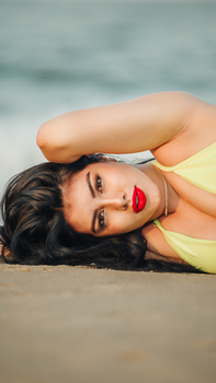 A beautiful woman with red lips poses on the sandy beach in a vibrant bikini.