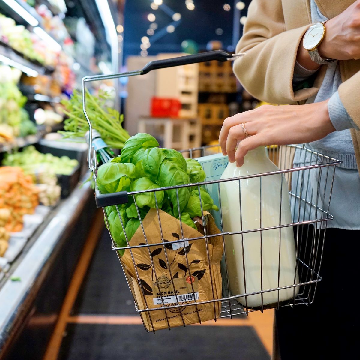 Cesta metálica de la compra con albahaca fresca y una botella de leche en un supermercado