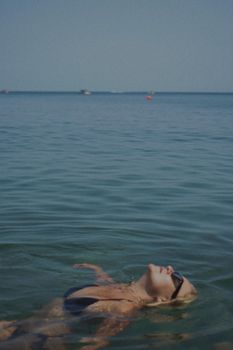 A woman in sunglasses floats peacefully in the tranquil sea under the daytime sky.