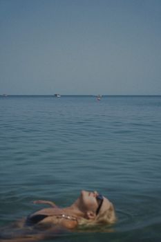 A woman floats peacefully in the ocean under a clear blue sky, capturing the essence of summer relaxation.