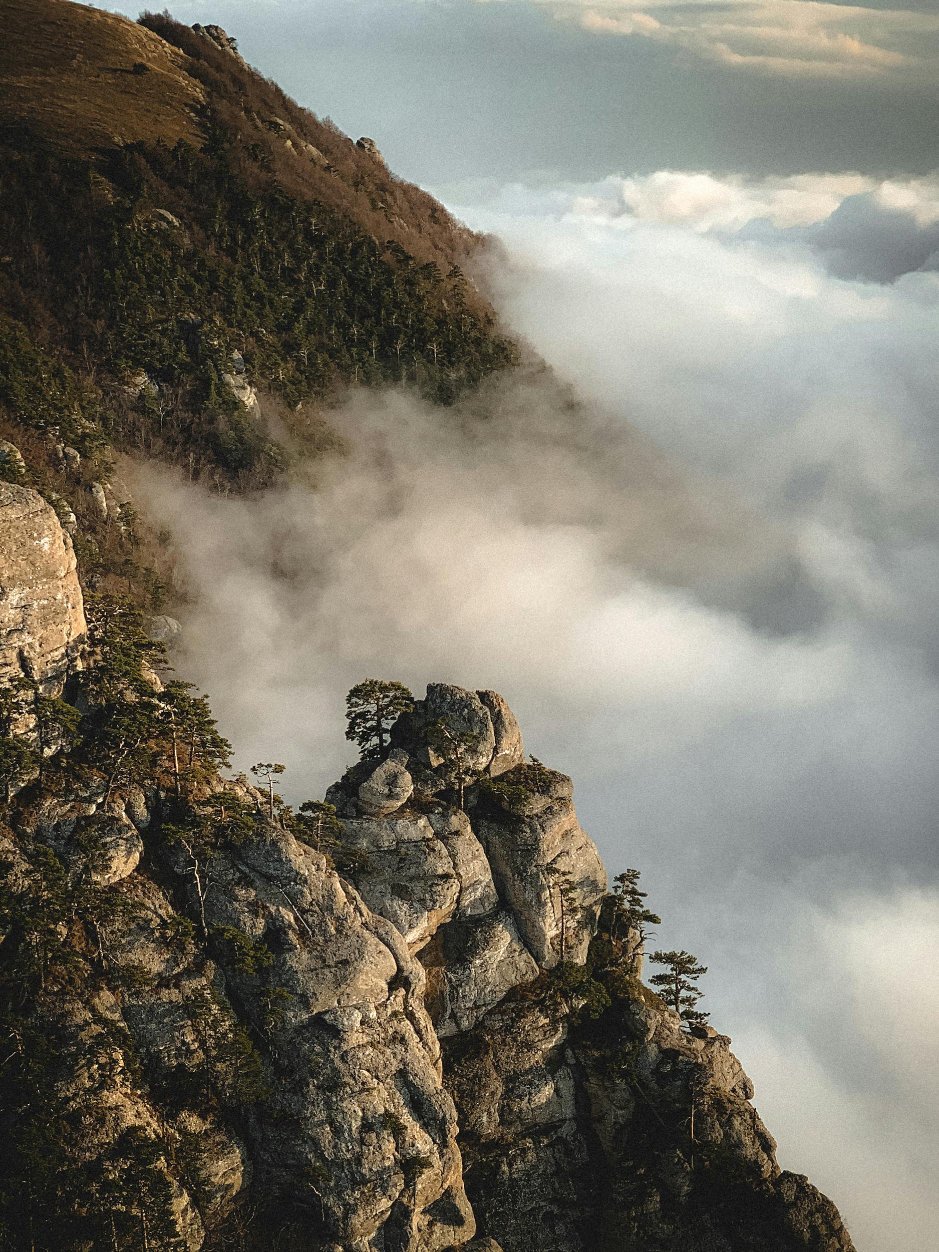 A breathtaking mountain landscape with rocky cliffs emerging through a sea of clouds under a soft, warm light.