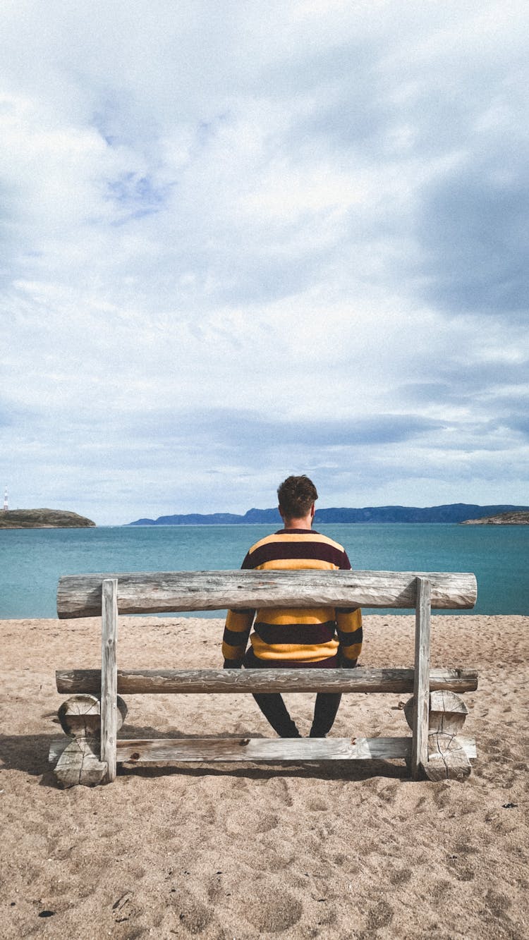 Backside Of A Man Sitting On A Bench Looking At The Sea