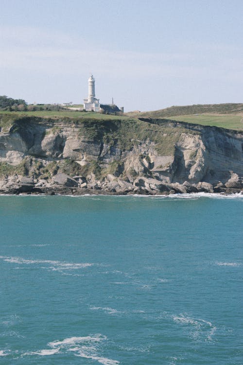 A Lighthouse on the Cliff Near the Body of Water