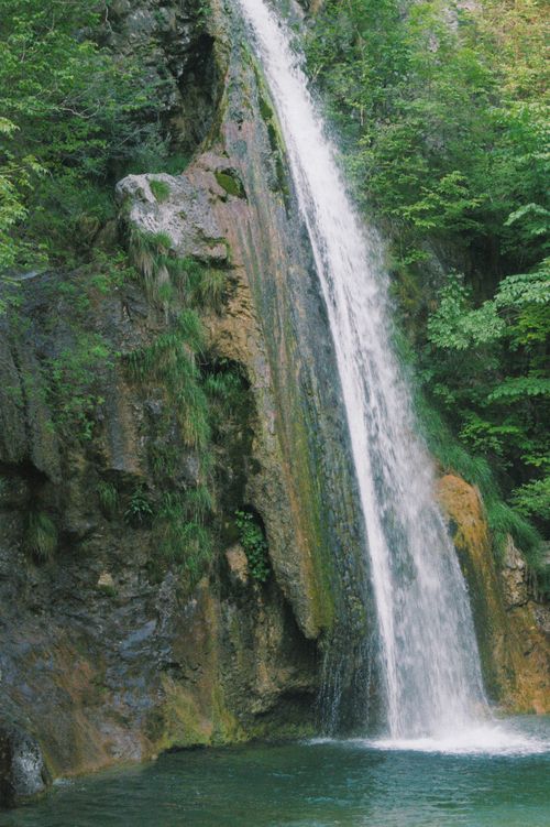 Free A serene waterfall cascading down rocky cliffs surrounded by vibrant green foliage in a lush forest setting. Stock Photo