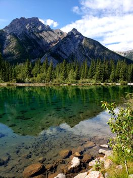 Scenic mountain view with clear lake and lush pines under a blue sky.