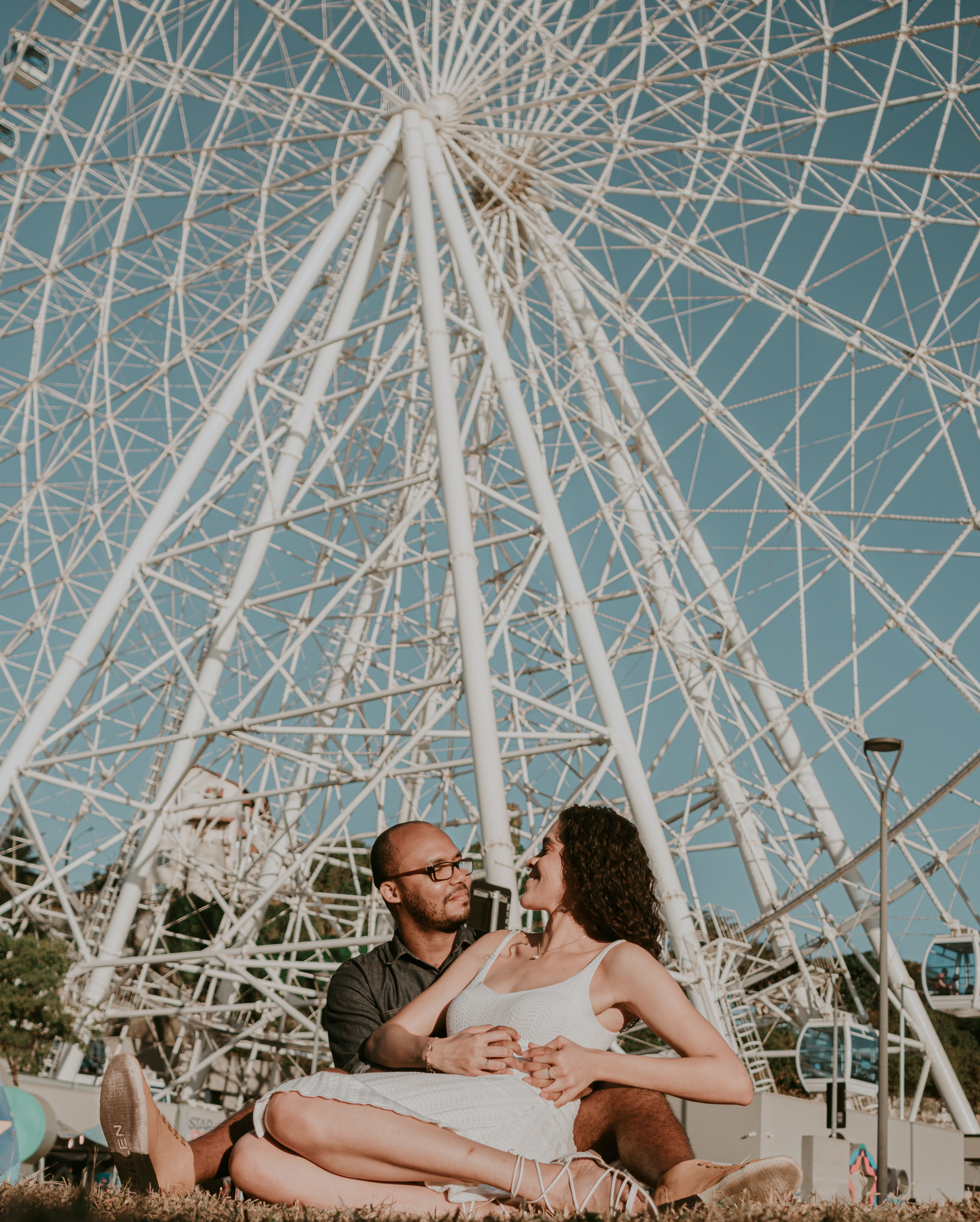 Couple enjoying a romantic moment sitting on grass with a giant ferris wheel in the background.