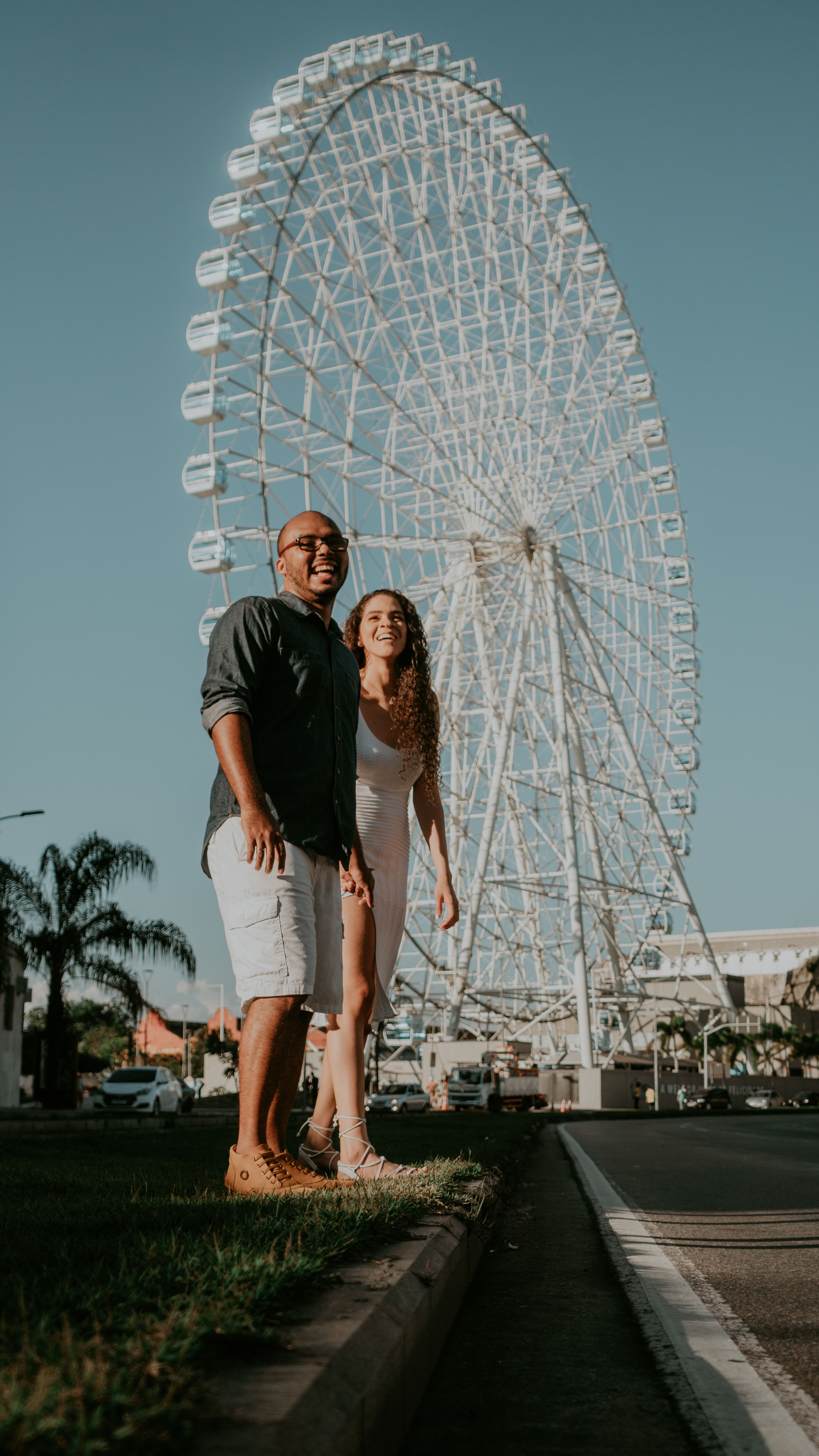 Happy couple enjoying a sunny day with a ferris wheel backdrop.