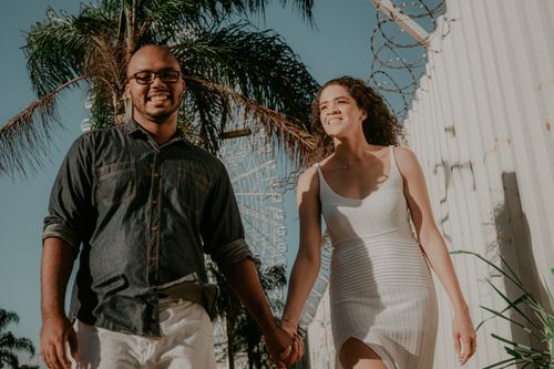 Free A cheerful couple holding hands and walking outdoors on a sunny day, expressing joy and togetherness. Stock Photo