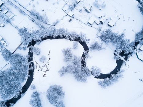 Aerial view of snowy Russian village with winding river and trees in winter.