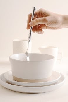 An elegant hand stirring a spoon in a bowl on a minimalist breakfast table setting.