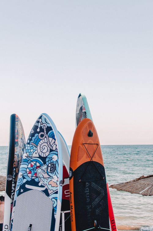 Free A vibrant collection of surfboards standing on a sandy beach by the ocean, capturing a sunny seascape. Stock Photo