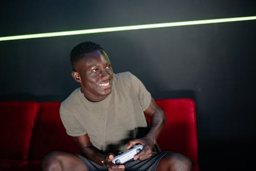 Black man sitting and playing video games with a controller indoors.