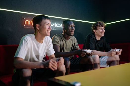 Three friends enjoy gaming together indoors, smiling and engaged with controllers.