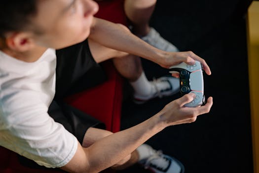 A young man plays video games, holding a wireless controller indoors, focused and relaxed.