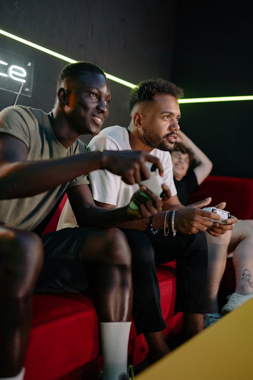 Men Sitting on Red Couch Playing a Video Game
