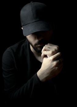 Close-up of a man in black attire with a contemplative pose on a dark background.