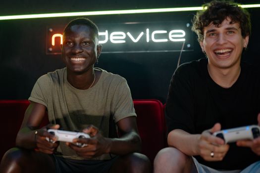 Two friends enjoying video games together indoors, smiling and holding game controllers.