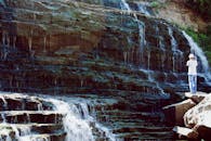 一个人穿着休闲装，站在瀑布边，捕捉着眼前的景象