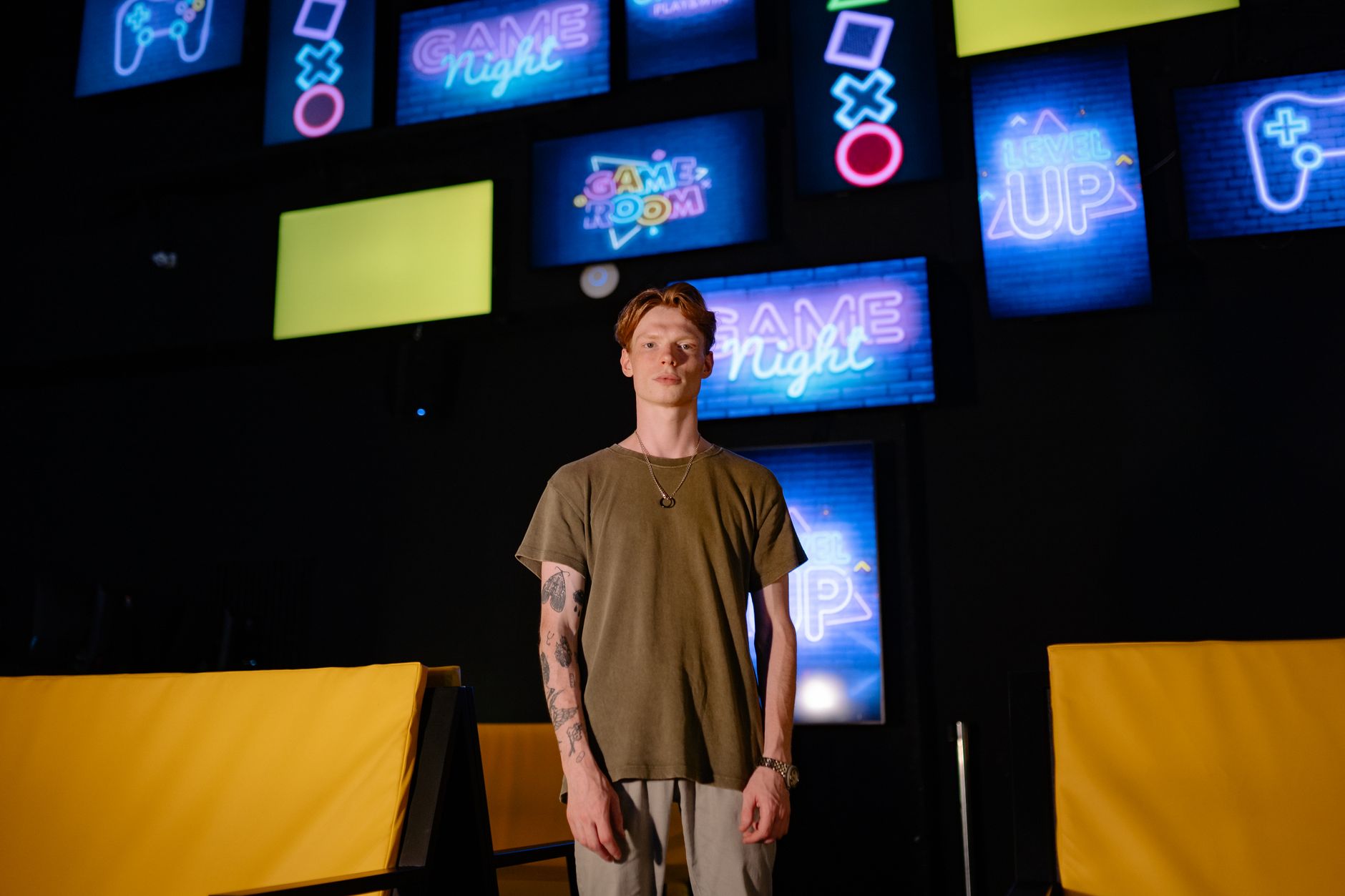 A young man stands in a game room, surrounded by colorful neon signs.