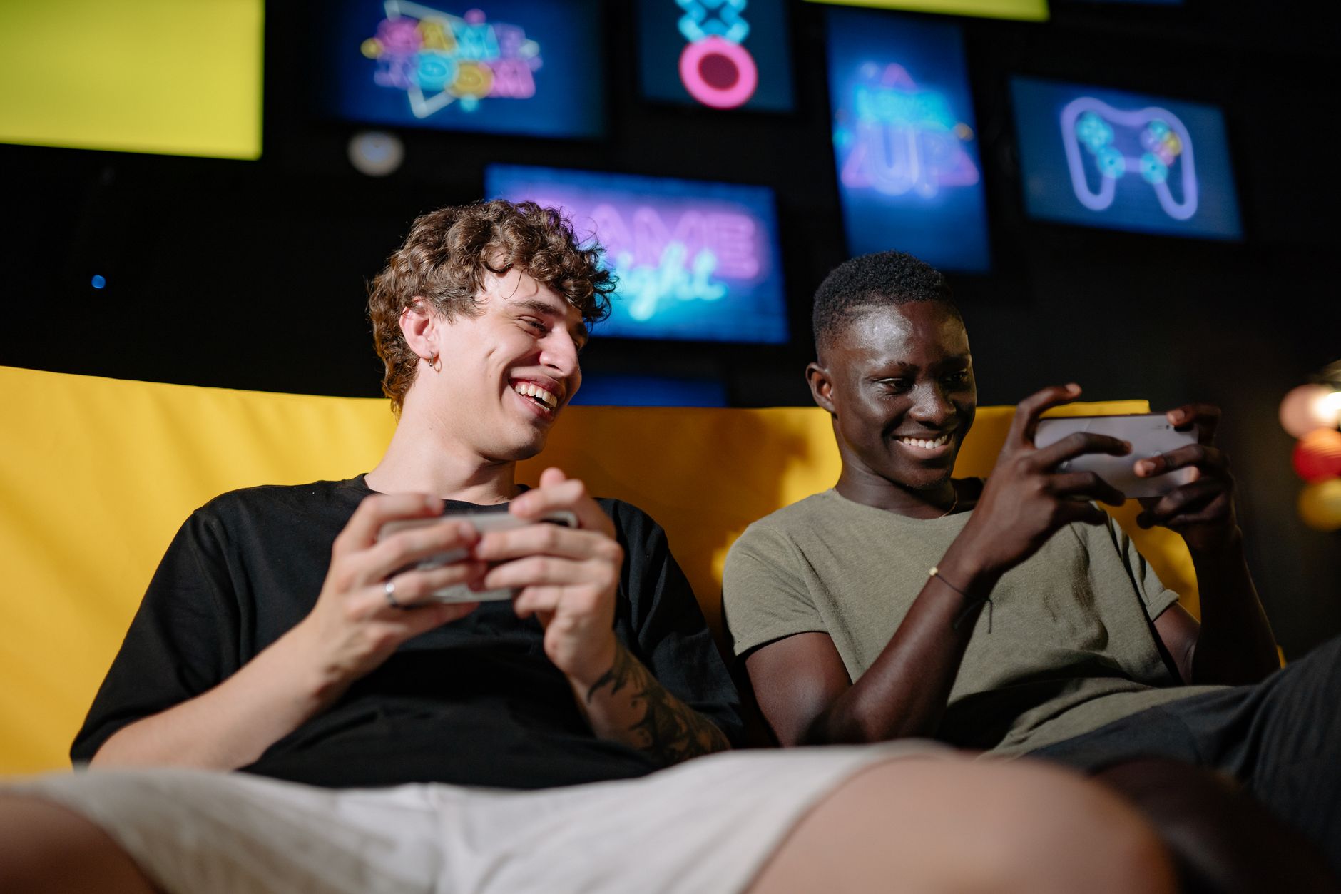 Two happy young men sitting together enjoying mobile gaming indoors.