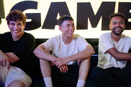 Three diverse young men laughing and enjoying their time together indoors.