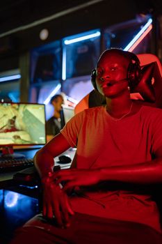 Portrait of a gamer wearing headphones in a neon-lit gaming arena, showcasing intense focus.