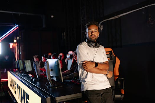 A confident gamer with headphones poses indoors by a row of gaming stations, arms crossed.