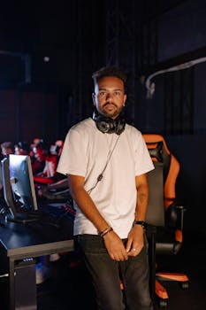 Young man standing in an esports room with a computer, engaged in gaming. Indoors with headphones.