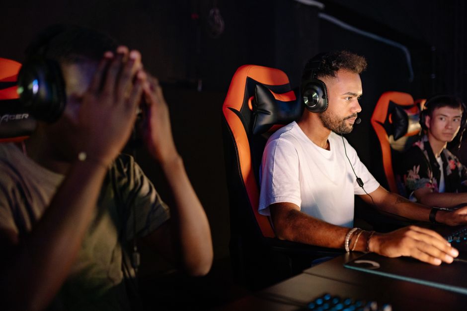 Three young men playing video games in an esports setting with headsets and gaming chairs.