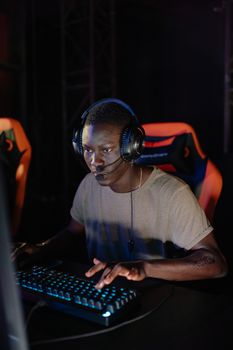 African American man fully immersed in online gaming with headset and keyboard.