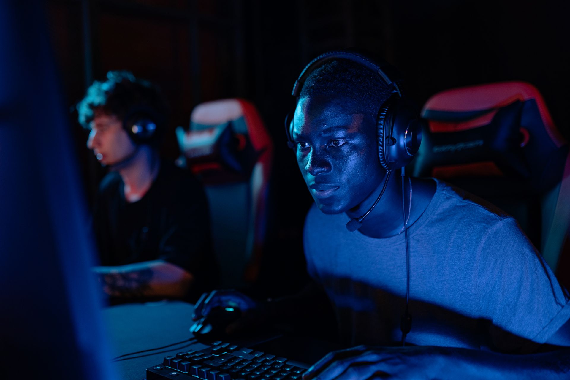 Two young men focused on gaming at computers, illuminated by blue light.