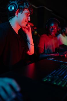 Two young men wearing headphones enjoying an esports session indoors, illuminated by colorful lighting.