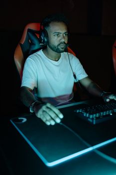 Man gaming with a headset and keyboard under neon lighting, showcasing focused intensity.