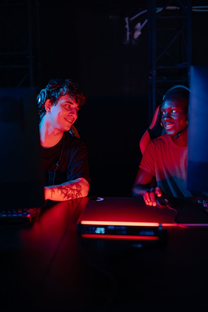 Two diverse friends enjoying a gaming session under vibrant lighting.
