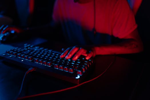 Focus on hands typing on an RGB gaming keyboard under ambient red and blue lighting.
