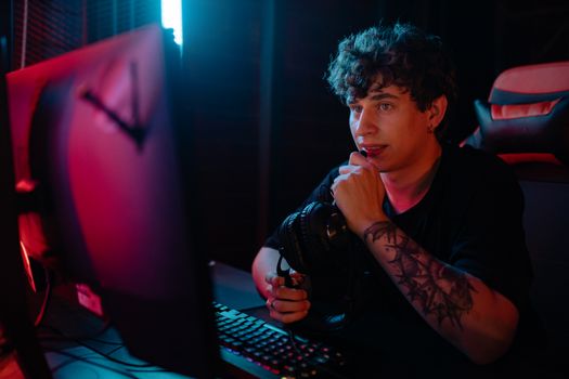A young man in a dimly lit room, focused on gaming with headphones and a computer setup.