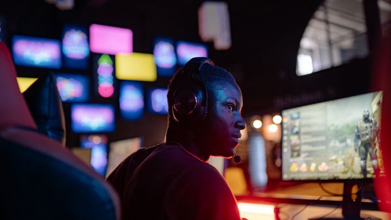 A young man intensely focused on a gaming session at a colorful gaming setup, wearing headphones.