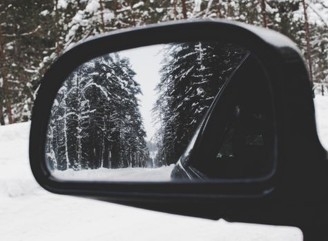 汽车后视镜中映出一片宁静的白雪皑皑的森林，捕捉了冬季旅行的精髓