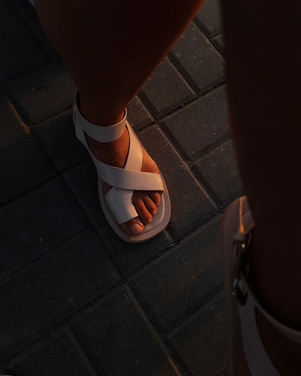 White leather sandals crossing sunlit pavement, capturing the ease of a pared-back summer outfit.