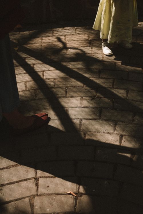 Free Children's feet casting playful shadows on cobblestone street under warm daylight. Stock Photo