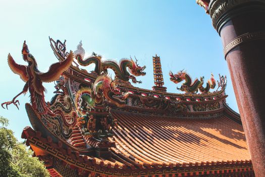 Traditional temple roof in Taipei adorned with colorful dragon sculptures under a clear blue sky.