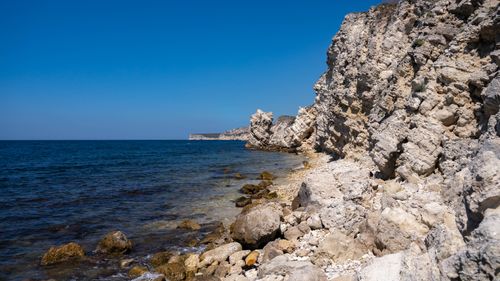 Free Beautiful rocky cliffs by the seaside with a serene ocean view and clear blue sky. Stock Photo