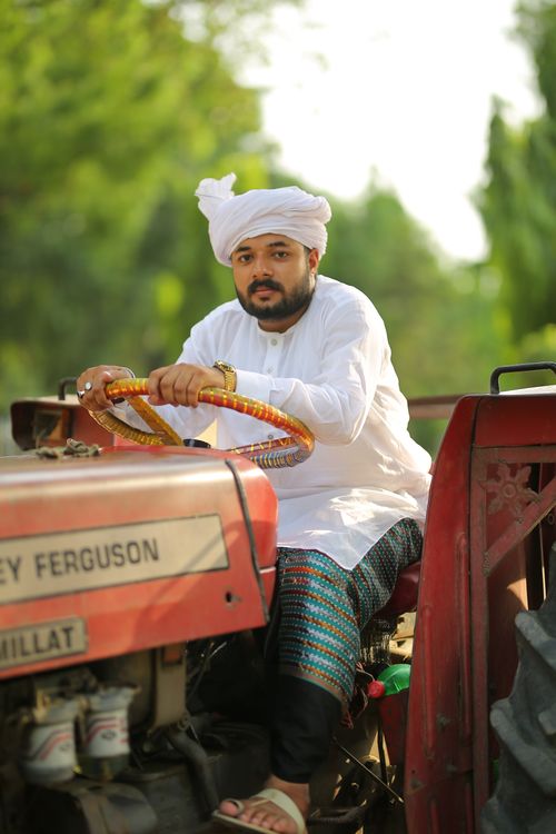 Free South Asian farmer in traditional clothing driving a tractor outdoors in Lahore. Stock Photo