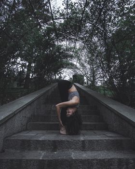 A woman performing a yoga pose on a staircase in a lush outdoor setting, showcasing flexibility and balance.