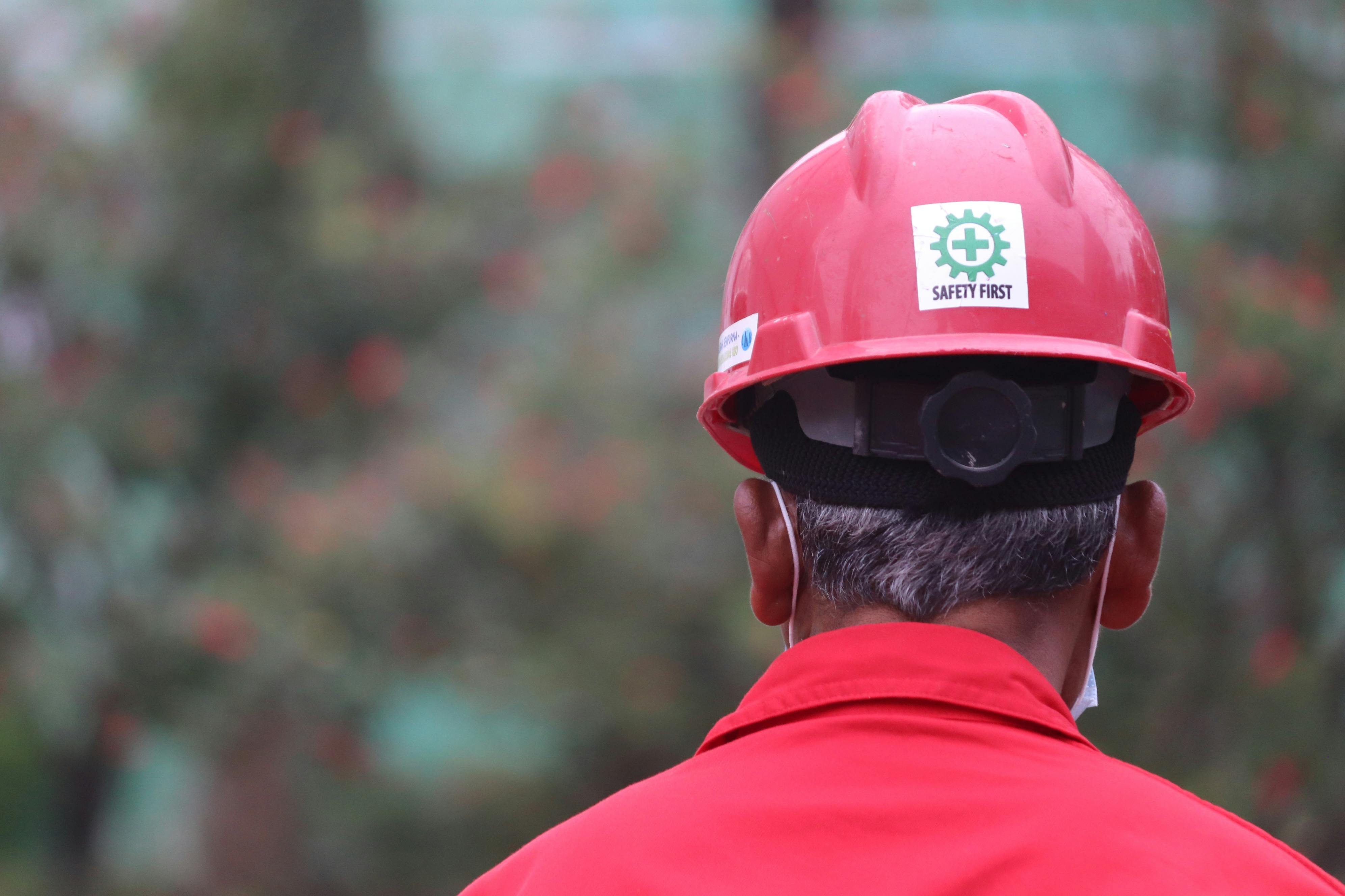 A worker focusing on safety outdoors, wearing a red helmet with a safety logo.