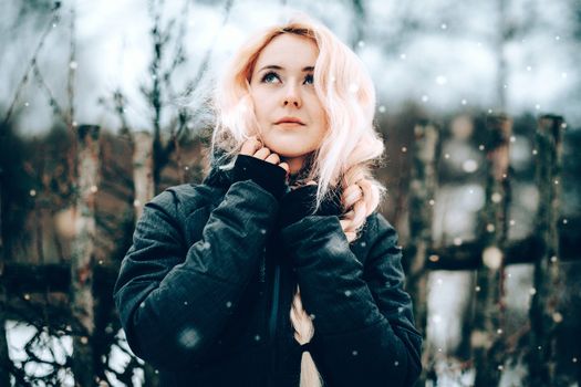 Portrait of a young blonde woman in a black jacket enjoying a snowy winter day outdoors.